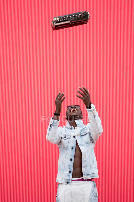 Verspielter afrikanisch-amerikanischer Mann wirft altes Radiogerät auf rotem Hintergrund — Stockfoto