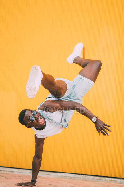African american man in denim jumpsuit practicing break dance on yellow background — Stock Photo