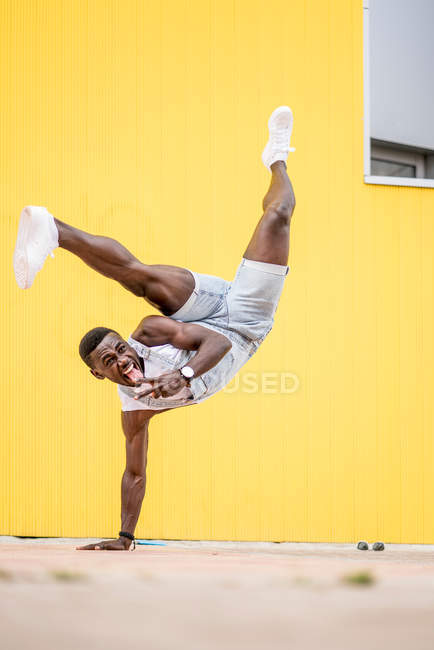 Homme afro-américain en combinaison de denim pratiquant break dance sur fond jaune — Photo de stock