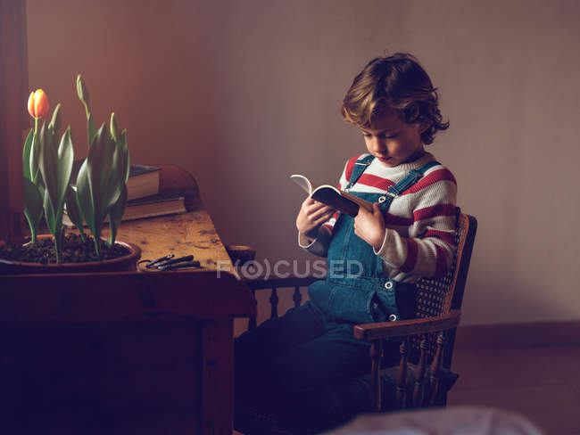 Garçon lecture livre à la table — Photo de stock