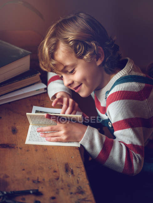 Garçon lecture livre à la table — Photo de stock