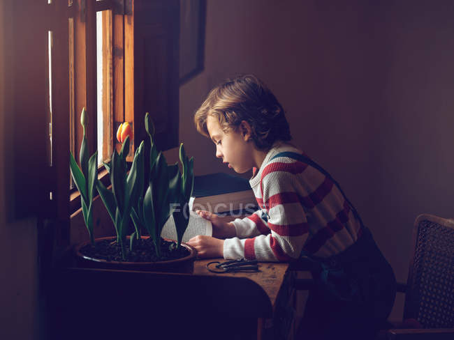 Vista laterale di giovane ragazzo carino seduto e lettura libro a tavola a casa — Foto stock