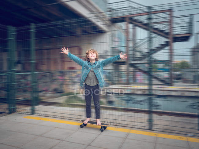 Chico descalzo divertido en monopatín con manos en pie en la plataforma del tren - foto de stock