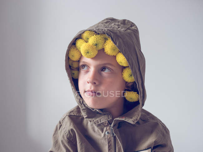 Niño reflexivo con flores en capucha sobre fondo blanco - foto de stock