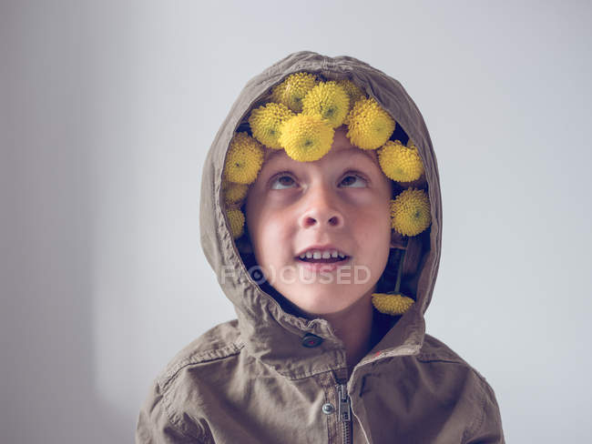 Fröhlicher Junge mit Blumen in Kapuze auf weißem Hintergrund — Stockfoto