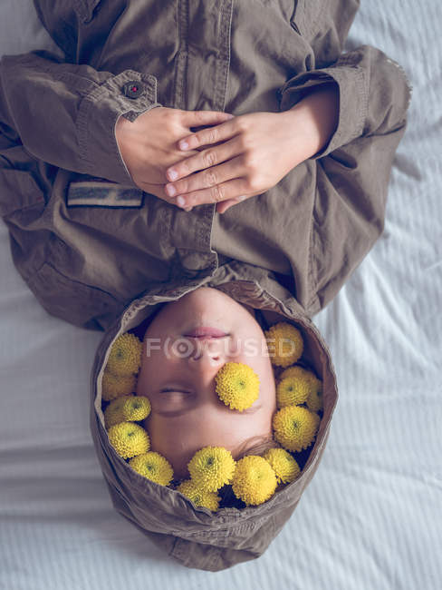 Спокойный симпатичный мальчик в венке из желтых цветов, лежащий на кровати — стоковое фото