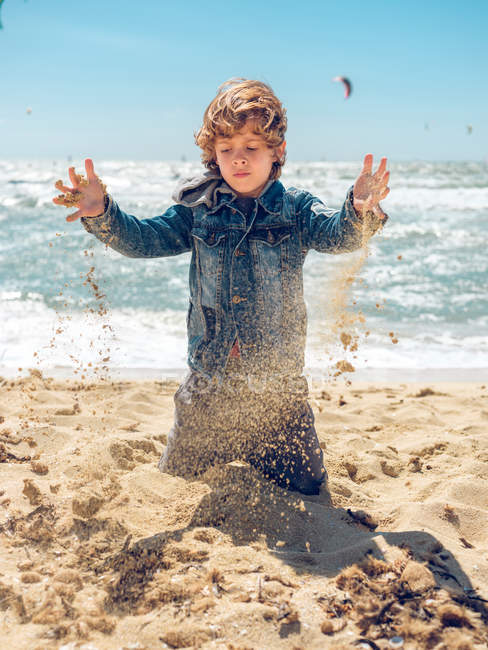 Хлопчик кидає пісок на узбережжі — стокове фото
