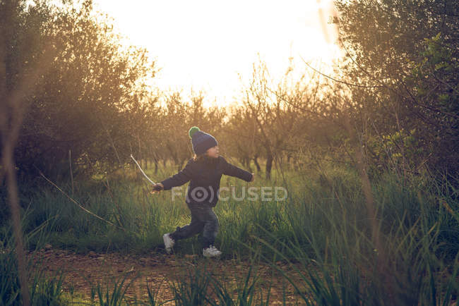 Side view of cute little boy running in nature and playing with stick — Stock Photo