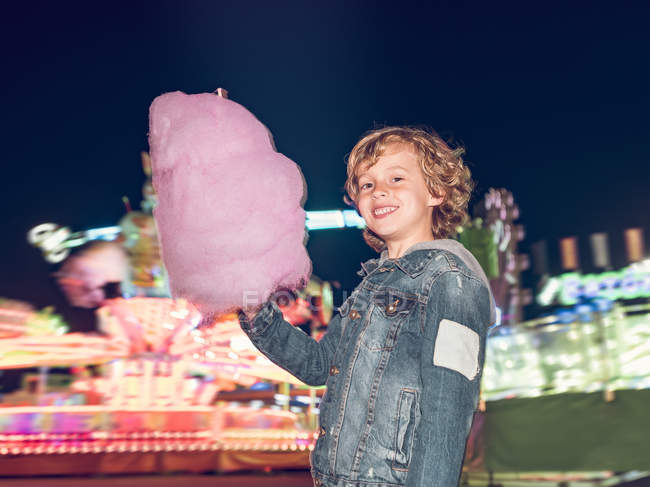Веселий маленький хлопчик стоїть з рожевою бавовняною цукеркою і дивиться на камеру — стокове фото