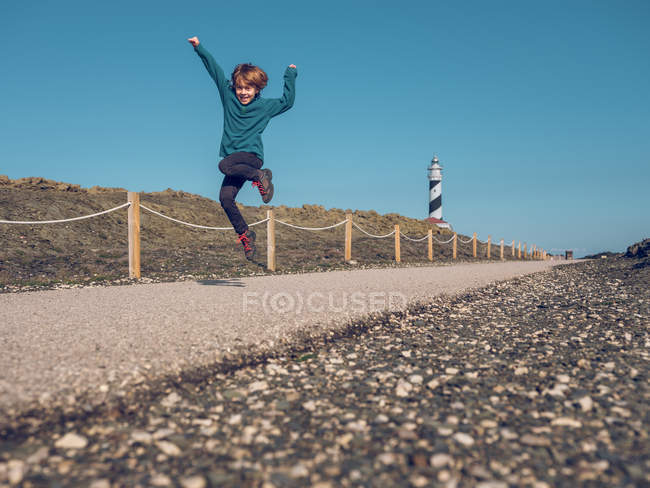 Cheerful boy jumping at lighthouse — Stock Photo