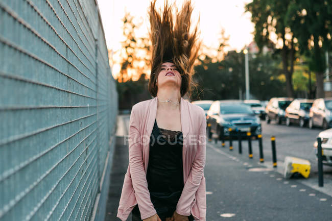 Attraente ragazza affascinante a piedi sulla strada vicino alle auto e scuotendo i capelli — Foto stock