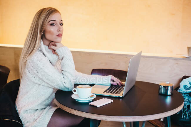 Senhora usando laptop na mesa com xícara de bebida e smartphone — Fotografia de Stock