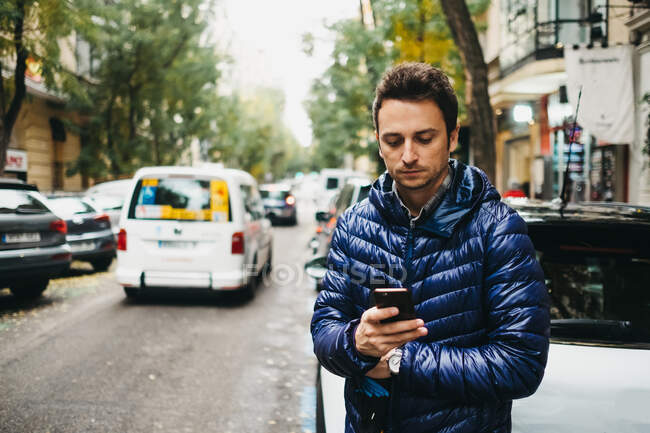 Молодой человек со смартфоном возле машин на улице — стоковое фото