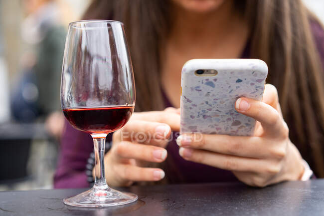 Crop jeune femme naviguant dans le téléphone mobile à table près d'un verre de boisson à Porto, Portugal — Photo de stock