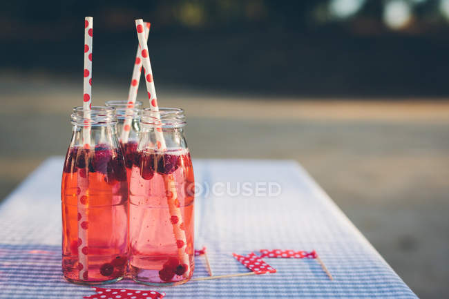 Bottles with fresh fruit drink and drinking straws on table outdoors — Stock Photo