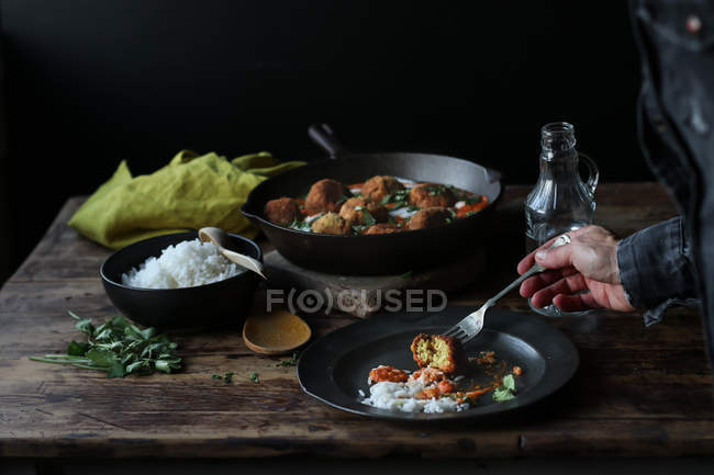 Hand of person taking cauliflower and quinoa ball with rice from plate on wooden table — Stock Photo