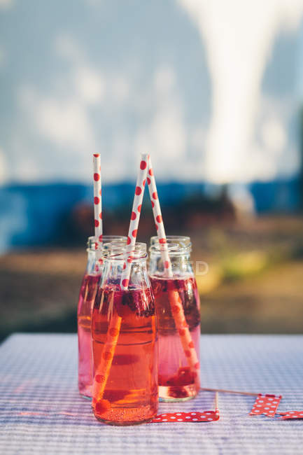 Bottles with fresh fruit drink and drinking straws on table outdoors — Stock Photo