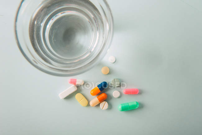 Різнокольорові таблетки та капсули зі склянкою води на білому тлі — стокове фото