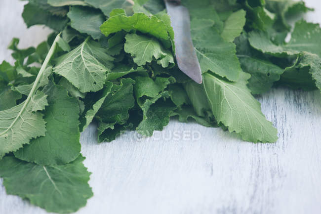 Knife on heap of green leaves on white wooden table — Stock Photo