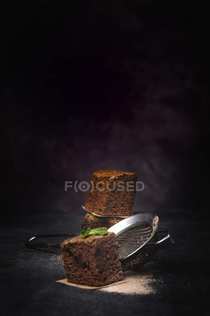 Pieces of chocolate brownie with mint on dark background with strainer — Stock Photo