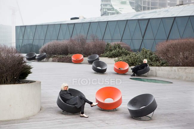 Women in dark wear sitting on abstract chairs near modern building in Lithuania — Stock Photo