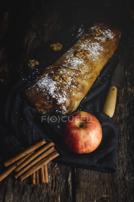Домашній яблучний штрудель з горіхами, родзинками та корицею на фоні темного дерева — стокове фото