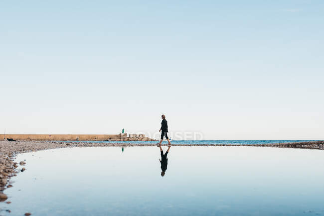 Seitenansicht einer anonymen Frau, die in der Nähe ruhigen Wassers gegen wolkenlosen Himmel in Altea, Spanien, spaziert — Stockfoto