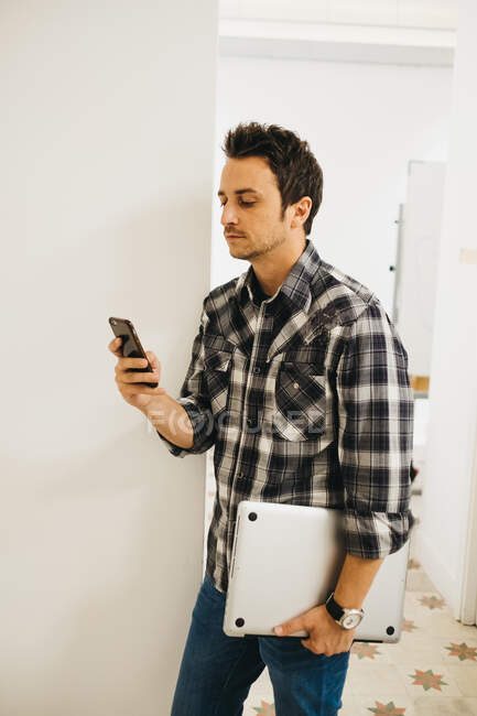 Jeune homme avec ordinateur portable navigation smartphone — Photo de stock
