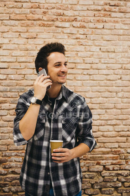 Jeune homme avec tasse parlant sur smartphone — Photo de stock