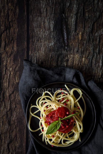 Spaghetti mit Tomatensauce und Basilikum auf Teller auf dunklem Holzgrund — Stockfoto
