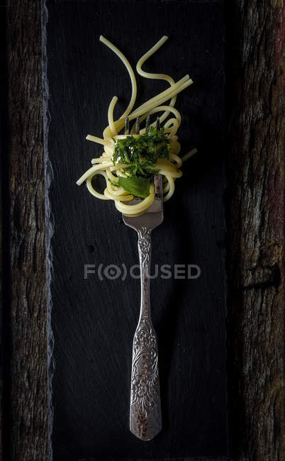 Spaghettis à la sauce pesto à la fourchette sur fond bois foncé — Photo de stock