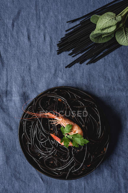 Black pasta with prawns served on black plate — Stock Photo