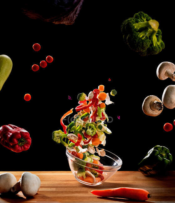 Высокоскоростная синхронизация миски с салатом, грибами, перцем и цветной капустой на черном фоне — стоковое фото