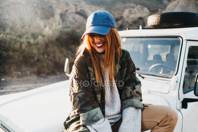 Young woman on casual wear sitting on car — Stock Photo
