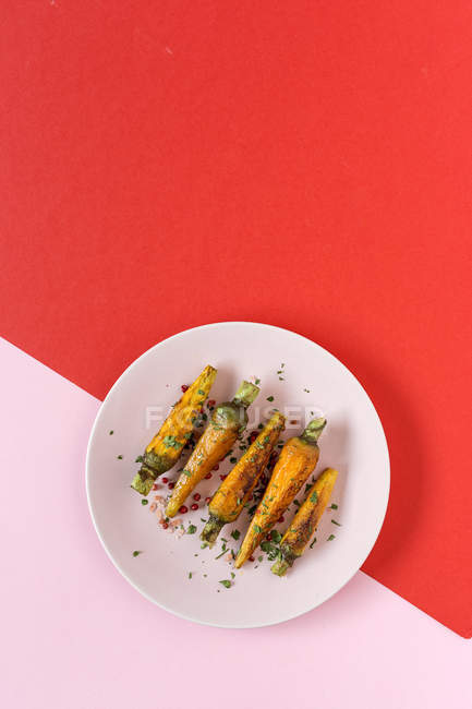Zanahorias asadas saludables con hierbas y especias sobre fondo rojo y rosa - foto de stock
