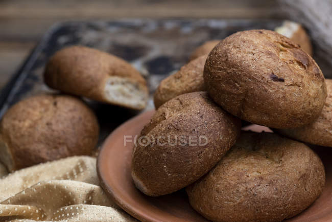 Fresh baked buns in heap on brown plate — Stock Photo
