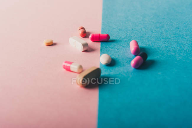 Pílulas e cápsulas espalhadas em fundo azul e rosa — Fotografia de Stock