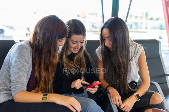 Senhoras atraentes a olhar para o telemóvel e sentadas em bancos na sala de espera do aeroporto do Porto, Portugal — Fotografia de Stock