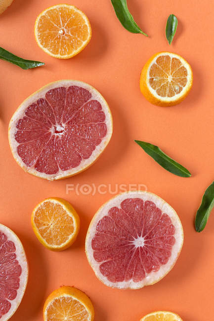 Rodajas de mandarina y pomelo con hojas verdes sobre fondo naranja - foto de stock