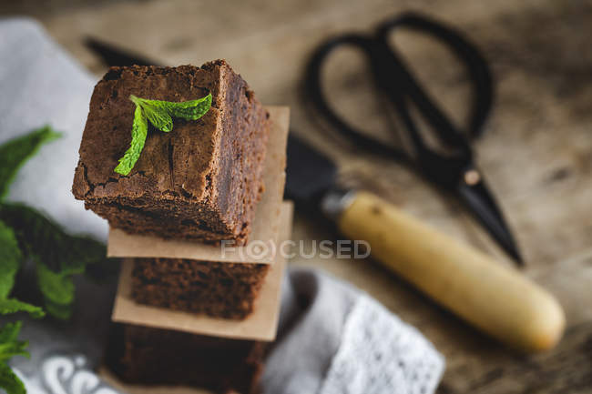 Stacked pieces of chocolate brownie with mint on wooden table — Stock Photo