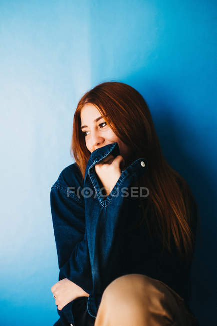 Mulher atraente sentada perto da parede azul — Fotografia de Stock