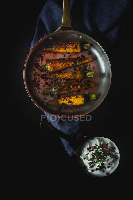 Healthy roasted carrots with herbs and spices on black background with sauce — Stock Photo