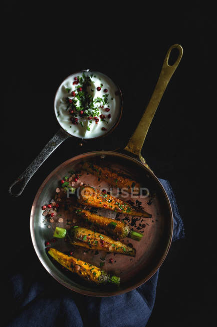 Cenouras assadas saudáveis com ervas e especiarias em fundo preto com molho — Fotografia de Stock