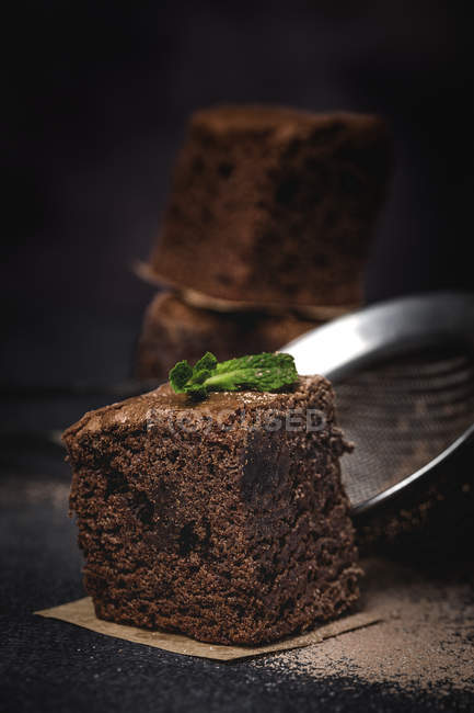 Pedazo de brownie de chocolate con menta sobre fondo oscuro con colador - foto de stock
