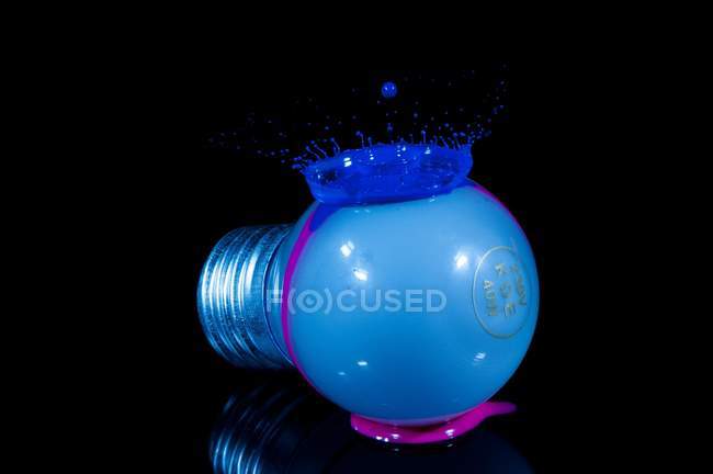 Blaue Flüssigkeit spritzt auf Oberfläche einer modernen Glühbirne auf schwarzem Hintergrund — Stockfoto