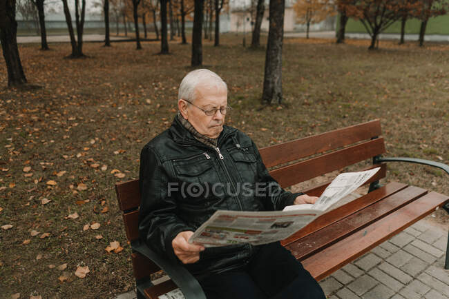 Літній чоловік читає газети в парку. — стокове фото