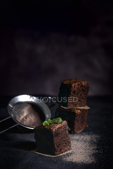 Кусочки шоколадного брауни с мятой на темном фоне со стрейнером — стоковое фото