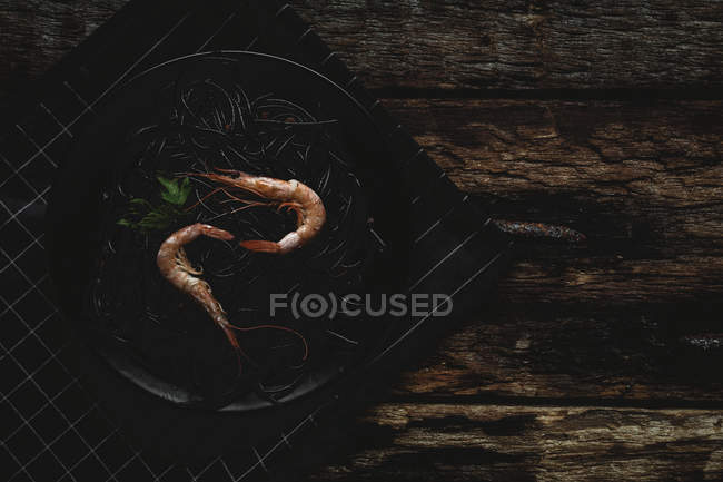 Pâtes noires aux crevettes servies sur une assiette noire sur une table en bois — Photo de stock