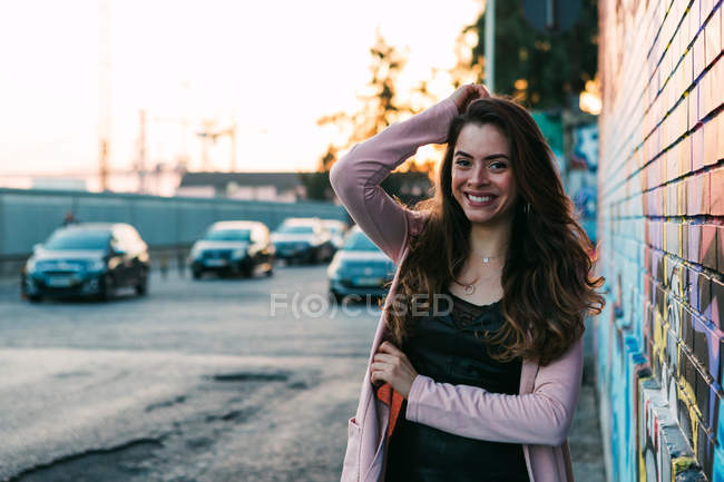 Attractive happy young woman with hand in hair standing on street — Stock Photo