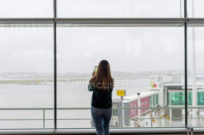 Voltar ver senhora atirando no telefone celular perto da janela na sala de espera do aeroporto no Porto, Portugal — Fotografia de Stock